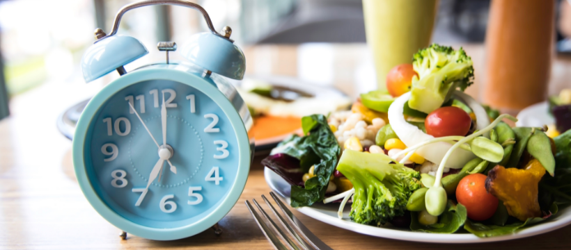 Billedet illustrerer tidsbegrænset faste, da der er et billede af et ur ved siden af en tallerken med mad